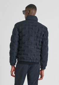 Giubbotto imbottito nero con cuciture orizzontali, colletto alto e polsini a costine. Presenta un design elegante e leggero. Vista posteriore mostrata.