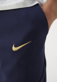 Marineblauwe sportbroek met een gladde structuur, voorzien van een prominent gouden Nike-logo aan de linkerkant.