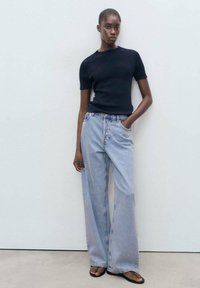 Svart stickad t-shirt med kort ärm, kombinerad med ljusblå vida denimjeans. Jeansen har hög midja och klassisk femficksdesign.