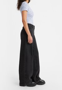 Tajt kortärmad topp i ljusblått med ett strukturerat mönster; högmidjade vida svarta jeans; kraftiga svarta platåskor.