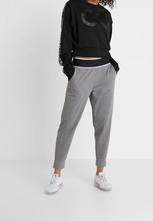 Sweatshirt noir court avec un grand logo, pantalon de survêtement gris fuselé avec poches, et chaussures de sport blanches. Tissu doux avec une coupe décontractée.