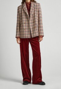 Blazer de doble botonadura en patrón de pata de gallo con tonos mezclados de beige, marrón y burdeos; combinado con pantalones de pana de pierna ancha en rojo oscuro.