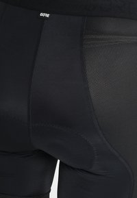 Pantalones cortos de ciclismo negros con textura suave, detalles de malla y una zona acolchada en el asiento; cintura con la marca "GORE".