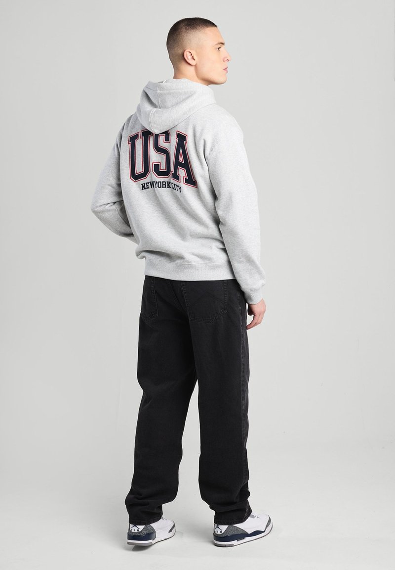 Gray hoodie with "USA NEW YORK CITY" in bold dark lettering on the back, paired with black pants and white shoes.