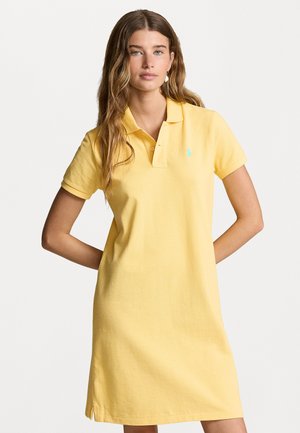 Polo jurk in zachtgele katoen met korte mouwen, een klassieke kraag en een klein blauw logo op de linkerborst. Zijsplitten voor comfort.