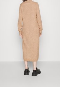 Robe pull beige tricotée, arrivant aux genoux, avec texture côtelée, manches longues et coupe décontractée. Assortie avec des chaussures noires épaisses.