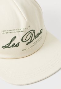 Cream-colored cap with a curved visor, featuring green embroidered text. It includes a logo and slogan, highlighting Scandinavian culture.