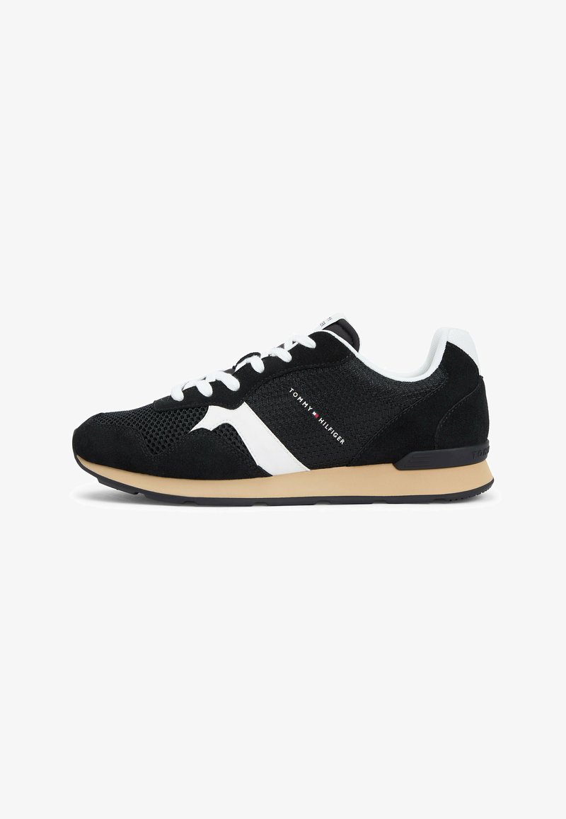 Baskets Tommy Hilfiger noires et blanches avec détails en mesh, semelle beige, lacets blancs, et logo de la marque sur le côté et le talon.