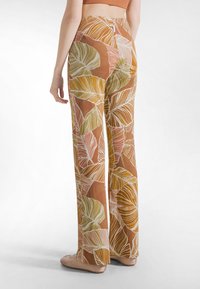 Spodnie z szerokimi nogawkami w ziemistym brązie z liściastym wzorem w zieleni i bieli, wykonane z lekkiego materiału, z wysokim stanem i luźnym krojem.