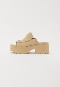 Beige suède platform sandalen met een open teen, dikke tussenzool en gestructureerde buitenzool. Heeft een eenvoudig ontwerp en een zichtbaar UGG-logo.