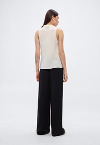 Αμάνικη μπλούζα σε κρεμ απόχρωση με γιακά, συνδυασμένη με χαλαρά μαύρα παντελόνια. Λείο ύφασμα με διακριτική λάμψη, άνετη σιλουέτα.