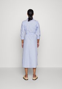 Gestreepte jurk in lichtblauw en wit, met een ceintuur in de taille, puffed sleeves en een knielange snit. Soepele stof met een knoopsluiting bij de kraag.