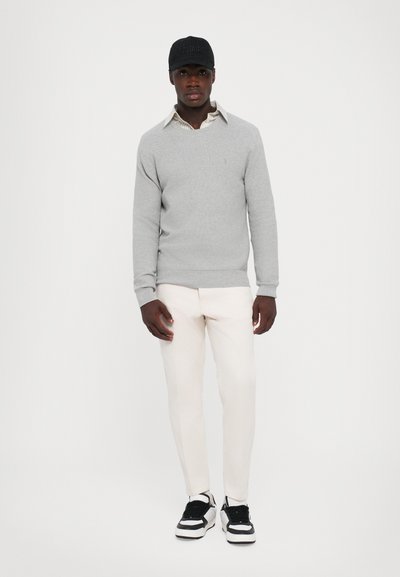 Suéter gris, pantalones crema, gorra negra con "VOLTAIRE" y zapatillas en blanco y negro. Diseño simple con textura acanalada en el suéter.