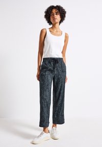 Pantaloni neri a fantasia con vestibilità comoda, vita con cordoncino e tasche laterali, abbinati a un top senza maniche bianco e sneakers bianche.