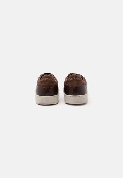 Paire de baskets en cuir marron avec semelles blanches vues de dos sur un fond uni clair.