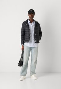 Puffer jacket in black, button-down blue and white striped shirt, light blue wide-leg jeans, white sneakers, and a black cap.