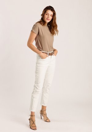 Haut beige à manches courtes associé à un jean blanc taille haute, rehaussé par une ceinture marron et des sandales à talons hauts beiges à brides.