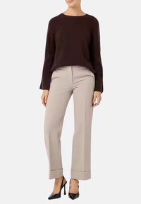 Maglione ribbed di un marrone scuro con maniche lunghe, abbinato a pantaloni beige chiaro a vita alta, con taglio dritto e polsini arrotolati. Tacchi neri.