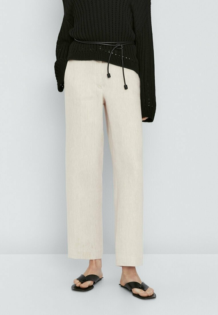 Zwarte gebreide trui met een losse pasvorm en een riem, gecombineerd met lichtbeige wijde broekspijpen en zwarte slipper sandalen. Gevoelige stofdetails zichtbaar.