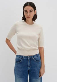 Helles beige Kurzarm-Strickoberteil mit rundem Halsausschnitt und geripptem Saum, kombiniert mit mittelblauen Jeans aus Denim mit regulärer Passform.