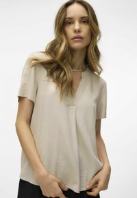 Blusa corta de manga corta en beige claro con escote en V, confeccionada en una suave tela texturizada. Ajuste casual, con un discreto detalle de costura.