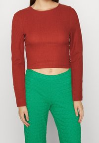 Crop top rosso a maniche lunghe con una texture a costine, abbinato a pantaloni verdi a vita alta con texture. Semplice scollo rotondo.