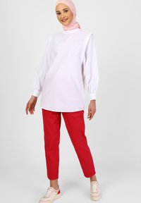 Weißes Langarmoberteil mit hohem Kragen, kombiniert mit roten lässigen Hosen und weißen Sneakers. Der Look zeichnet sich durch weichen Stoff und einen lockeren Schnitt aus.