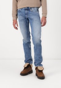 Lichtblauwe denim jeans met een slim fit, vervaagde textuur, vijf zakkenontwerp en een knoopsluiting, gecombineerd met bruine veterschoenen.
