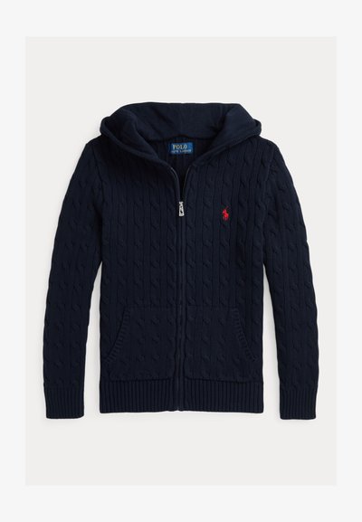 Jūras zilas krāsas adīts džemperis ar rāvējslēdzēju priekšpusē, kapuci un divām priekšējām kabatām. Iespēlēts mazs sarkans logo kreisajā krūtīs. Strukturēts audums.