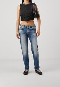 Svart ärmlös topp med rynkade sidor, blå raka jeans med blekning och fem fickor, kombinerat med svarta låga klackskor och en handväska.