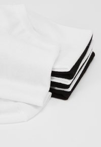 Vier Paare Crew-Socken, zwei weiße und zwei schwarze. Der Stoff ist unifarben, mit einer glatten Textur und standardisierten gerippten Bündchen.