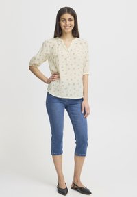 Lichte, crèmegekleurde blouse met watermeloenprint, korte pofmouwen en een V-knopen halslijn, gecombineerd met blauwe cropped jeans en zwarte ballerina's.