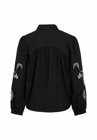 Blouse noire à manches longues avec empiècement dos froncé, manches bouffantes, et broderie florale blanche sur les deux manches.