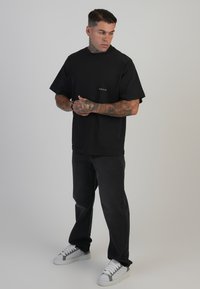 Crna pamučna majica kratkih rukava s malim bijelim logom. U paru s tamnim trapericama i bijelim tenisicama s sivim akcentima.