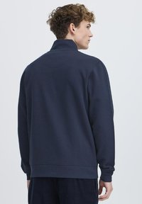 Marineblå, bomullspullover med høy krage, ribbede mansjetter og kant. Glatt tekstur, minimalistisk design, ingen synlige logoer eller mønstre.