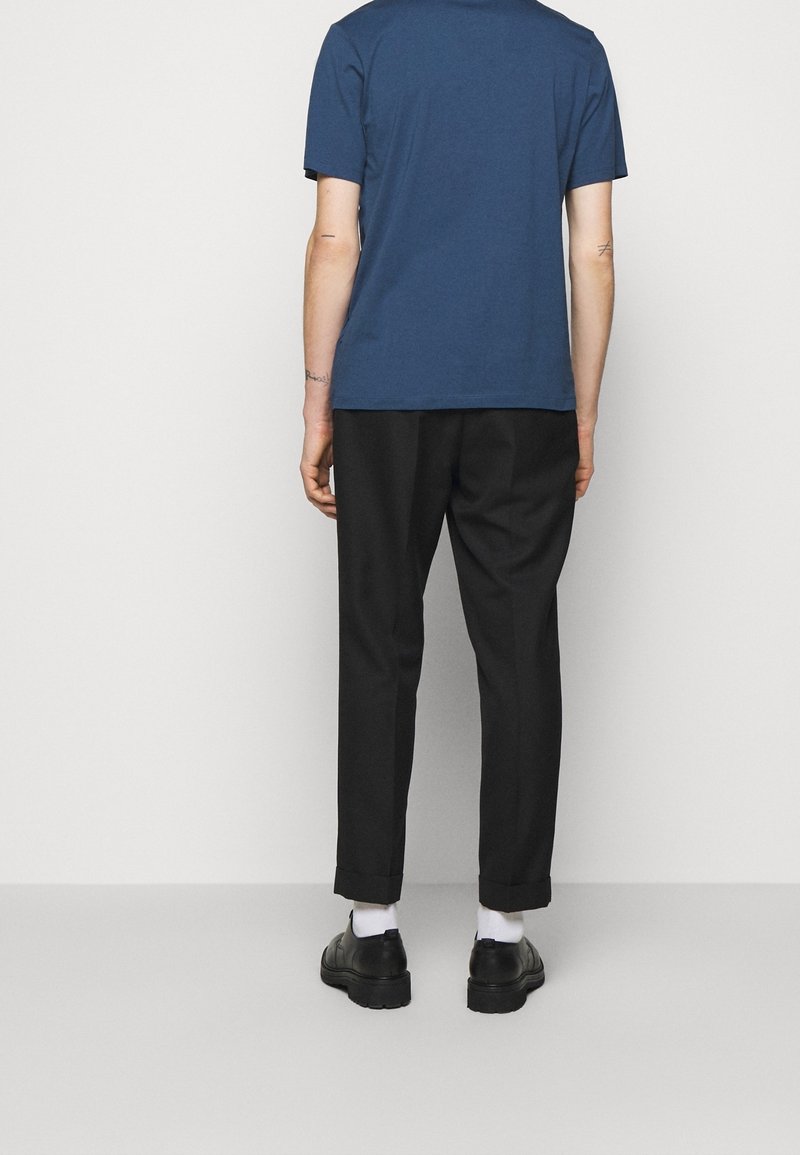 Granatowa koszulka z krótkim rękawem w zestawieniu z czarnymi, podwiniętymi spodniami oraz czarnymi butami, z białymi skarpetkami widocznymi na kostkach.