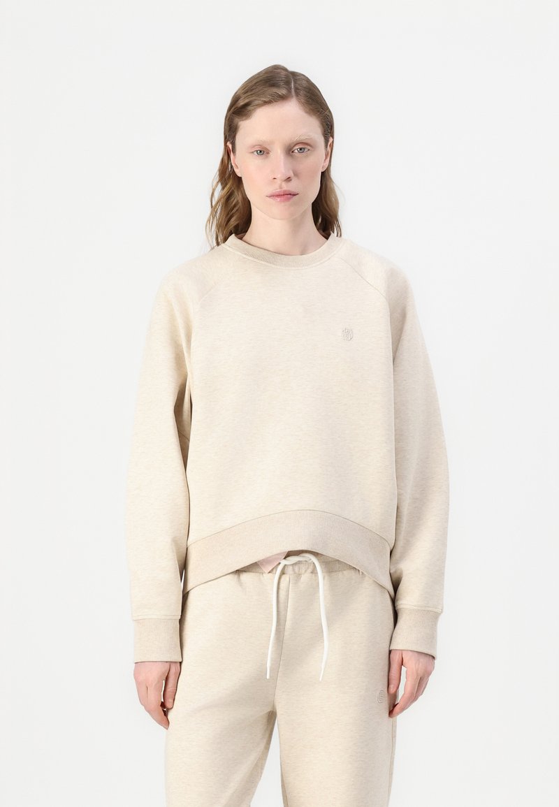 Beige fleece tröja med rund hals, ribbade ärmslut och fåll. Har en liten logotyp på bröstet och en avslappnad passform.