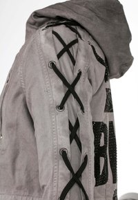 Grau Jacke mit Kapuze, dekorativer Schnürung mit schwarzen Schnüren an den Ärmeln und strukturierten Akzenten mit einem gemusterten Design auf der Vorderseite.