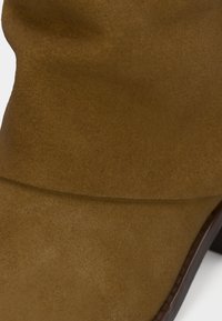 Barna velúr bokacsizma sima textúrával, lekerekített orral és vastag sarokkal. A szárán enyhén hajtott kialakítás található.