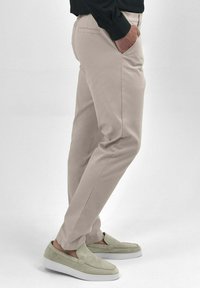 Beige chino's gemaakt van een katoenmix, met zijzakken en een getailleerde pasvorm. Draagt met lichtgrijze instap schoenen.