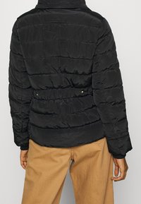 Černá zateplená bunda s prošívanými panely, páskem v pase a vysokým límcem. Hladký, lesklý materiál s elastickými manžetami a lemem.