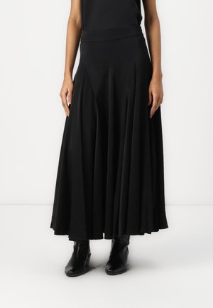 Gonna maxi nera realizzata in tessuto elastico, con vita elastica e design svasato con pieghe, abbinata a stivaletti neri.