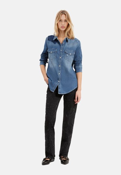 Camisa de mezclilla azul claro con botones y dos bolsillos en el pecho, diseño desgastado, y jeans oscuros con un patrón sutil, combinados con zapatos planos negros.