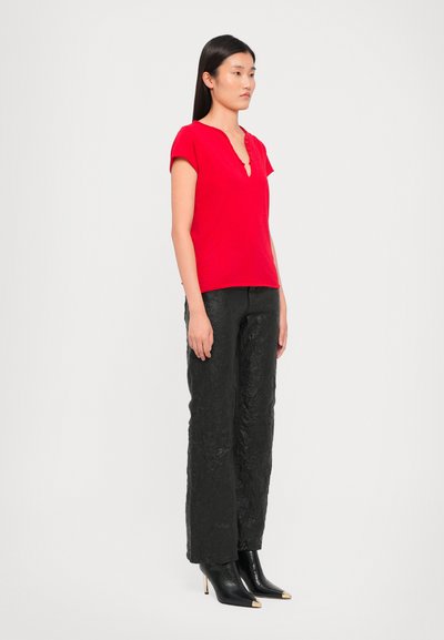 Red short-sleeve top with a V-neckline and button detail, paired with black textured wide-leg pants and pointed black ankle boots.