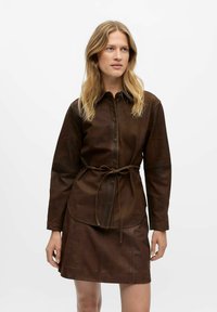 Brun læder skjorte med krave og knapfront, med langeærmer og bånd i taljen. Glat tekstur og tætsiddende design.