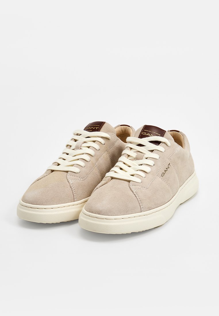 Beiga mockasin sneakers med vita gummisålar. Funktioner inkluderar snörning, vadderad tunga och märkesdetaljer på baksidan. Enkelt design.