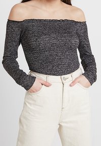 Schulterfreies Langarmtop aus schwarzem und grauem strukturiertem Strick, kombiniert mit hochtaillierten hellen Denim-Jeans.