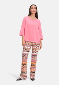 Rosa Langarmtop mit rundem Ausschnitt, kombiniert mit mehrfarbigen Hosen im Zickzackmuster mit schwarzen, rosa und orangefarbenen Akzenten.