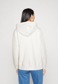 Witte oversized hoodie met een trekkoordcapuchon, geribde manchetten en zoom. De stof lijkt glad te zijn zonder zichtbare patronen of accenten.