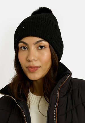 Gorro de punto acanalado negro con un pompón esponjoso en la parte superior. Presenta sutiles lentejuelas decorativas y un ajuste ceñido. Se lleva con una chaqueta acolchada oscura.
